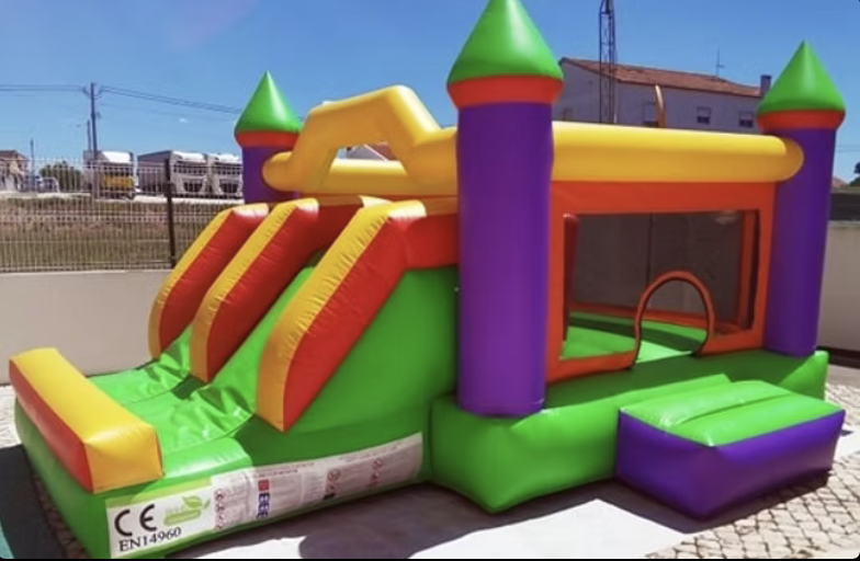 Insuflável Aladim em forma de castelo colorido com escorrega duplo verde, torres roxas e detalhes laranja e amarelo